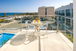 A balcony with a table and chairs, overlooking a swimming pool and a view of the sea.