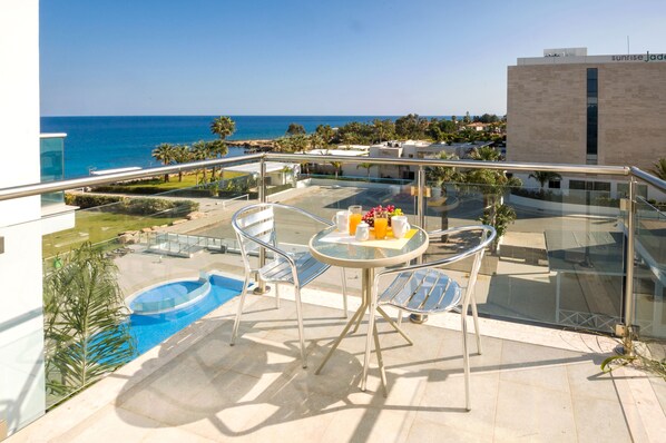 A balcony with a glass table, chairs, and a small pool.