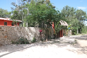 A stone wall with a thatched-roof structure, surrounded by lush greenery and trees.