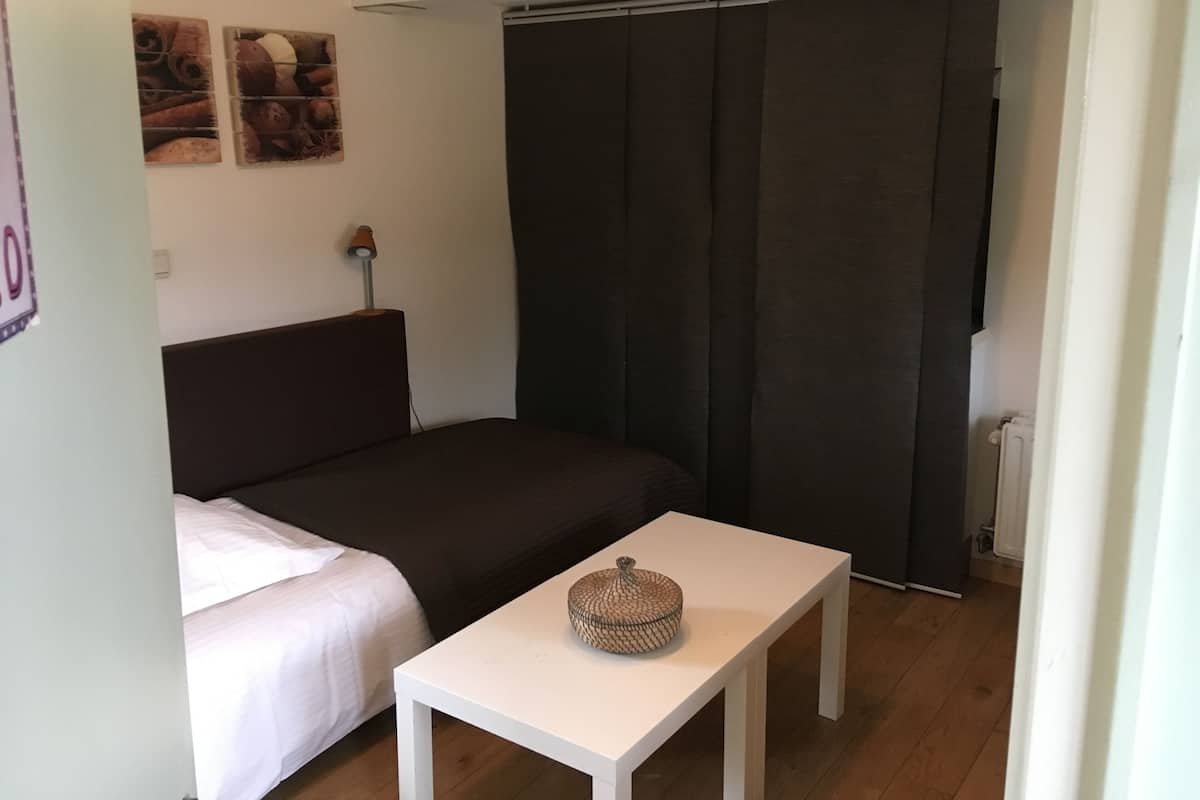 Una habitación pequeña y acogedora con una cama, una mesa blanca y un sofá oscuro.