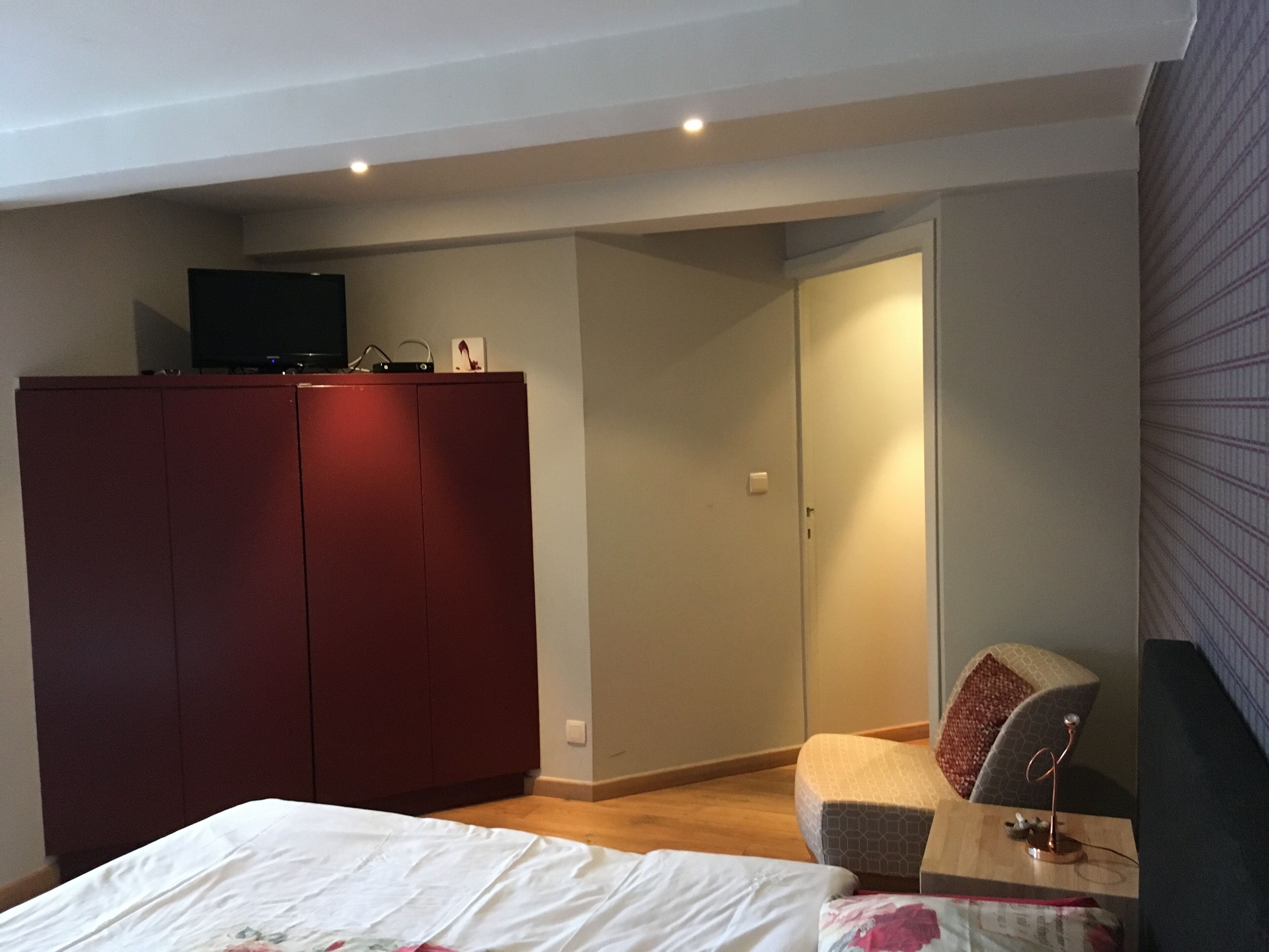 Un dormitorio con cama, armario, escritorio con lámpara y una silla.