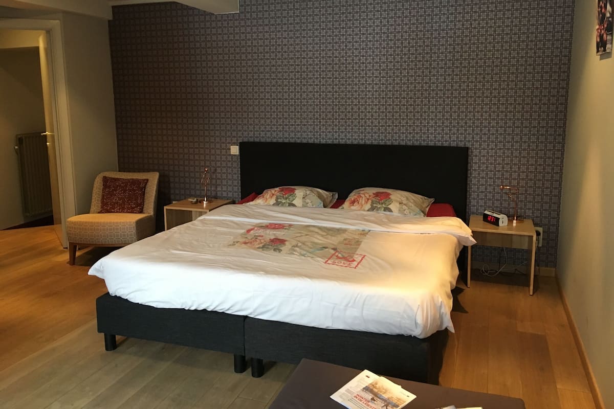 Un dormitorio ordenado con una cama grande, dos mesitas de noche, una silla y suelo de madera.