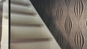 Una escalera con un muro decorado y barandilla de cristal.