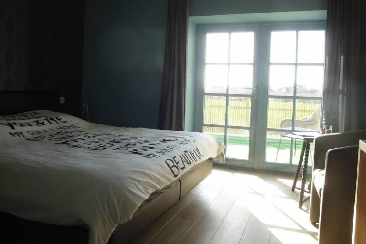 Un dormitorio con una cama grande, una ventana con cortinas y vista a una valla exterior.