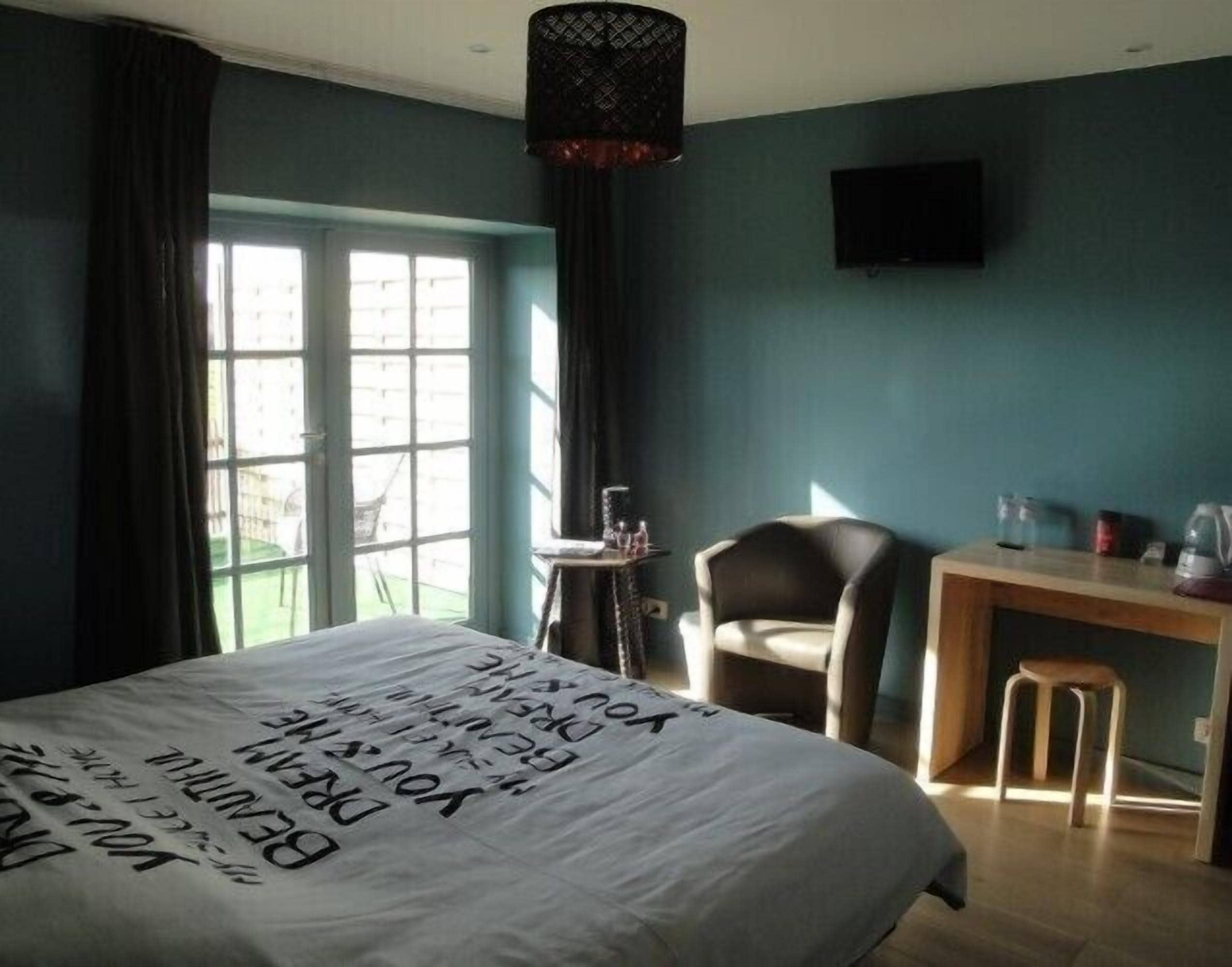 Een slaapkamer met een bed, een bureau, een stoel, een televisie en een raam met gordijnen.