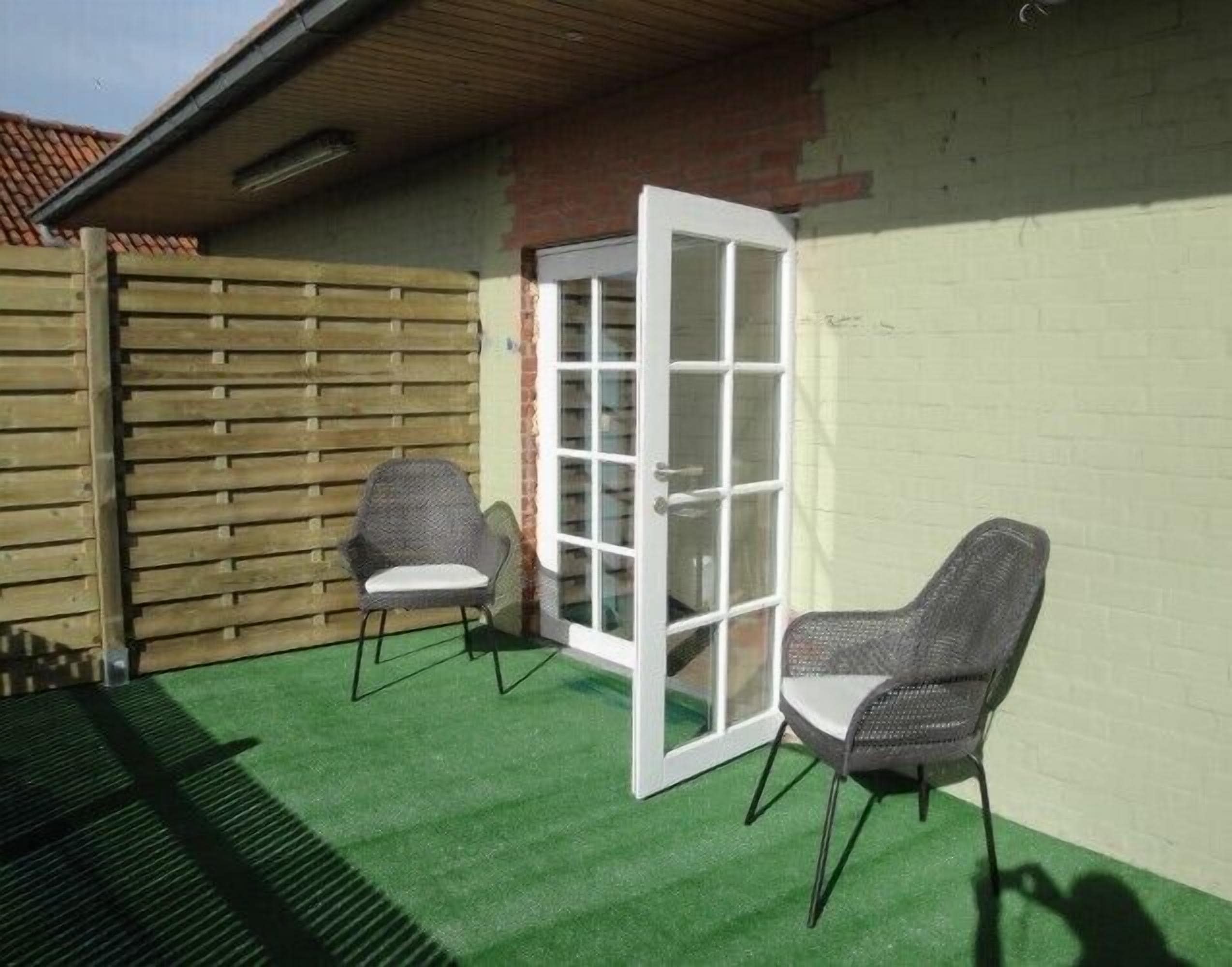 A small patio area with two wicker chairs, a white door, and a green artificial turf floor.