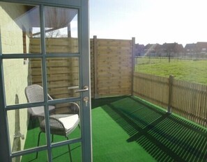 A balcony with a wicker chair, a wooden fence, and a green artificial turf. - De Zoete Kers B&B (Dentergem)
