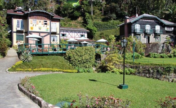 A traditional building with a balcony, surrounded by lush greenery and a stone wall.
