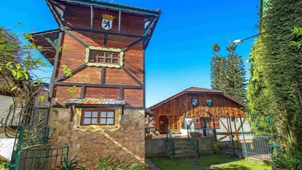 Un edificio tradicional de madera con base de piedra, sección superior de madera y una pequeña torre con un emblema de corona.