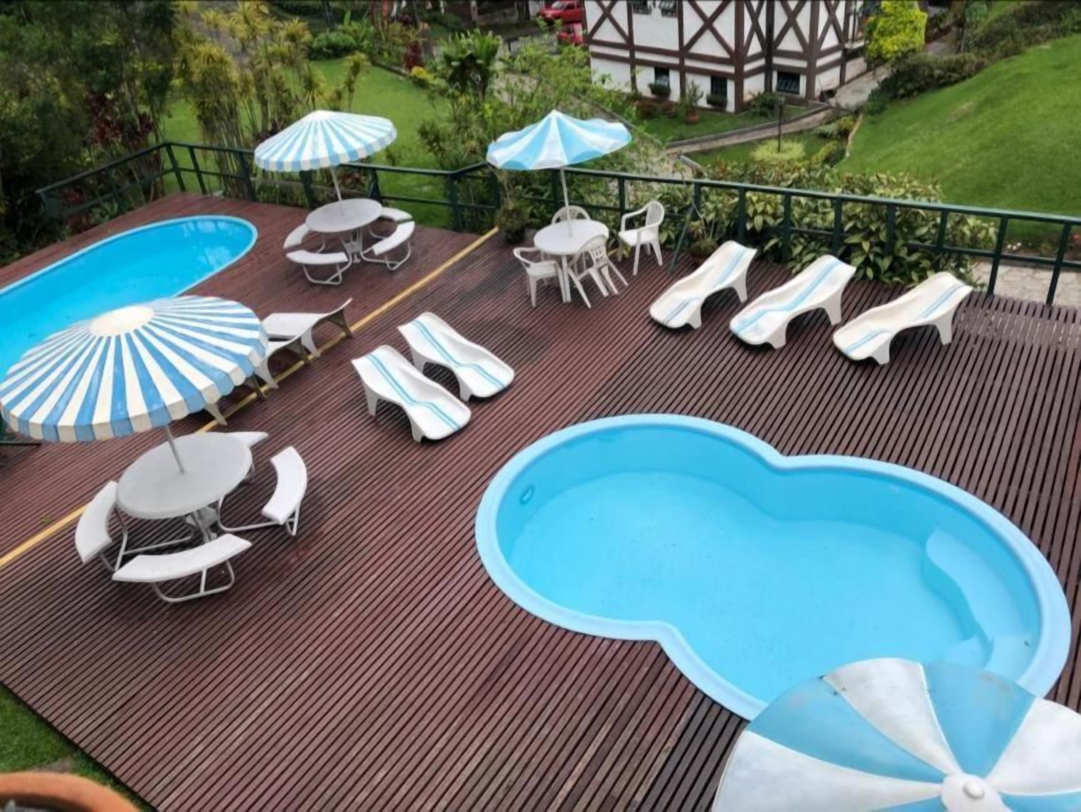 A pool area with lounge chairs and umbrellas, surrounded by a wooden deck and a garden.