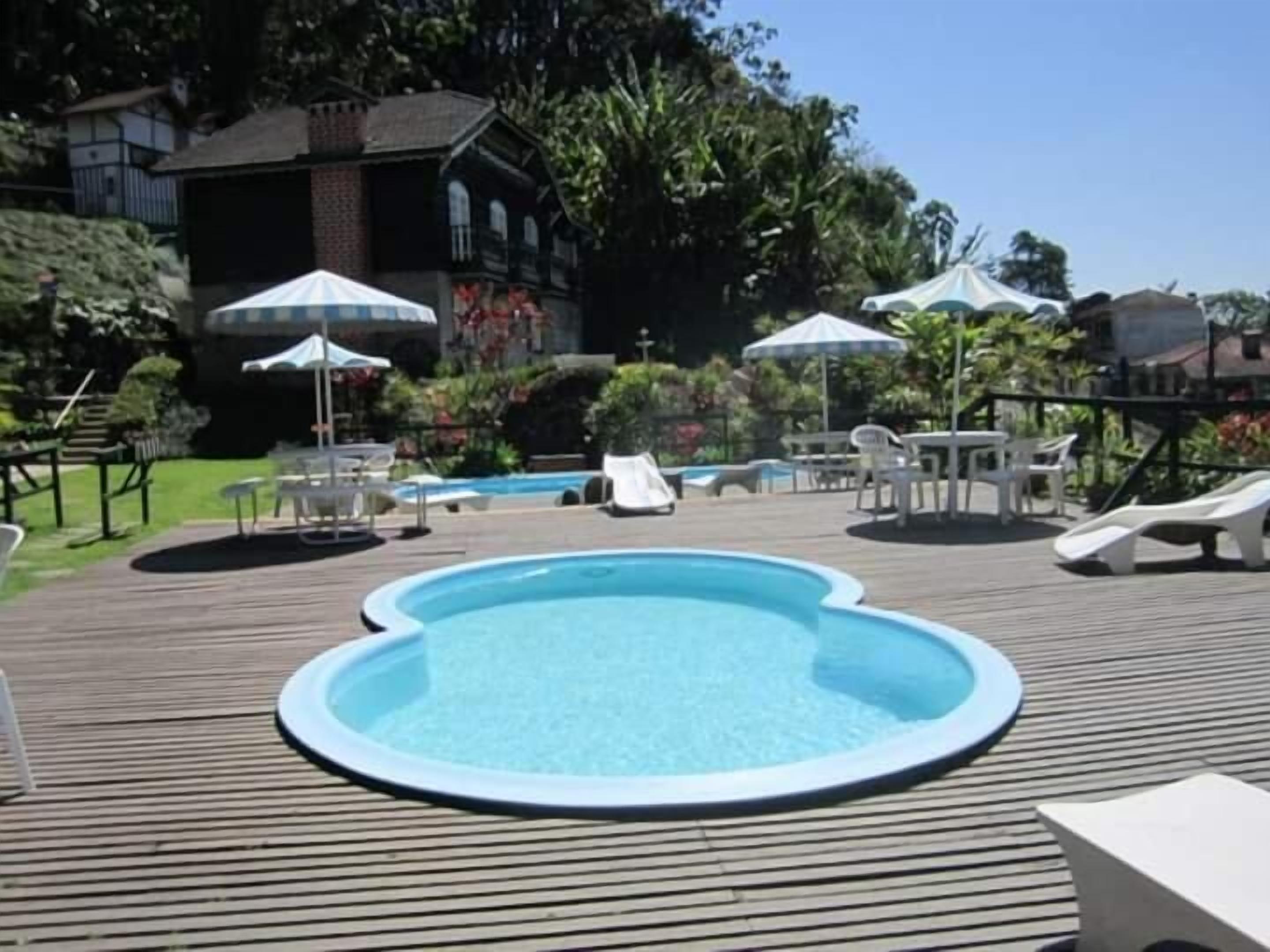 An outdoor swimming pool with a wooden deck, lounge chairs, and umbrellas.