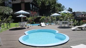Et udendørs swimmingpool med træterrasse, liggestole og parasoller.
