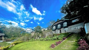 Una casa grande con fachada de piedra, múltiples ventanas y un jardín bien cuidado con césped y parterres de flores.