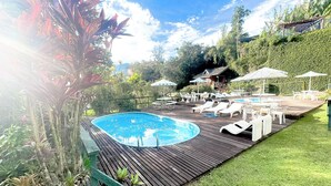 Un patio trasero con piscina, sillas de descanso y sombrillas.