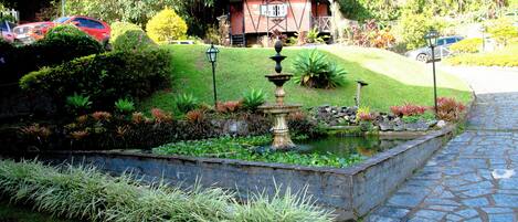 Um jardim com uma fonte, um caminho de pedra e uma casa ao fundo.