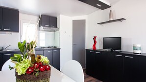 A modern kitchen with dark cabinets, a gas stove, and a flat-screen TV. - Superior Mobile Homes Kastanija - Campsite (Novigrad)