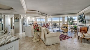 A spacious living area with a large window, a dining table, and a comfortable seating arrangement. - Gorgeous condo in Oceanfront Building + Free Attraction Tickets! (Myrtle Beach)