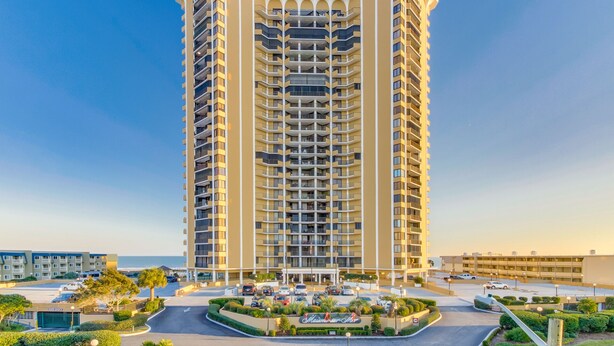 A tall, multi-story hotel with a central courtyard and a view of the sea. - Gorgeous condo in Oceanfront Building + Free Attraction Tickets! (Myrtle Beach)