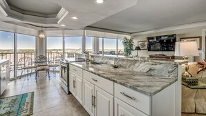 A spacious kitchen with a large island, white cabinetry, and a view of the desert landscape through large windows. - Gorgeous condo in Oceanfront Building + Free Attraction Tickets! (Myrtle Beach)