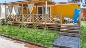 A wooden deck with a covered seating area, a small pool, and a yellow building with a blue door. - Camping Adria Mobile Homes Park Umag (Brtonigla)