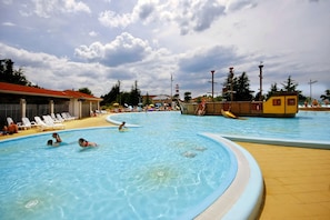 Piscina com água azul cristalina, rodeada por espreguiçadeiras e um deck de madeira.