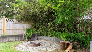 Un hogar de piedra rodeado por un muro de piedra curvo, con una valla de madera y abundante follaje al fondo.