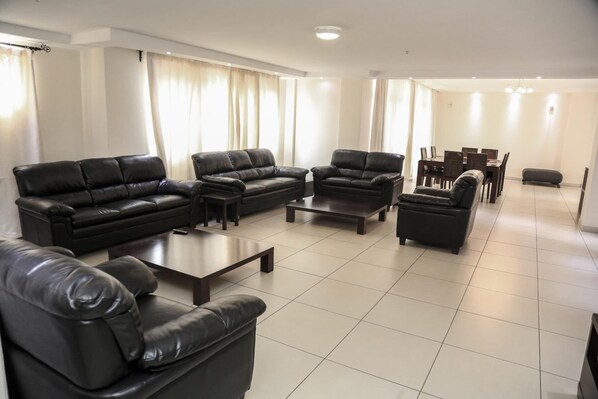 A spacious living room with a black leather sofa set, a coffee table, and a dining area with a table and chairs.