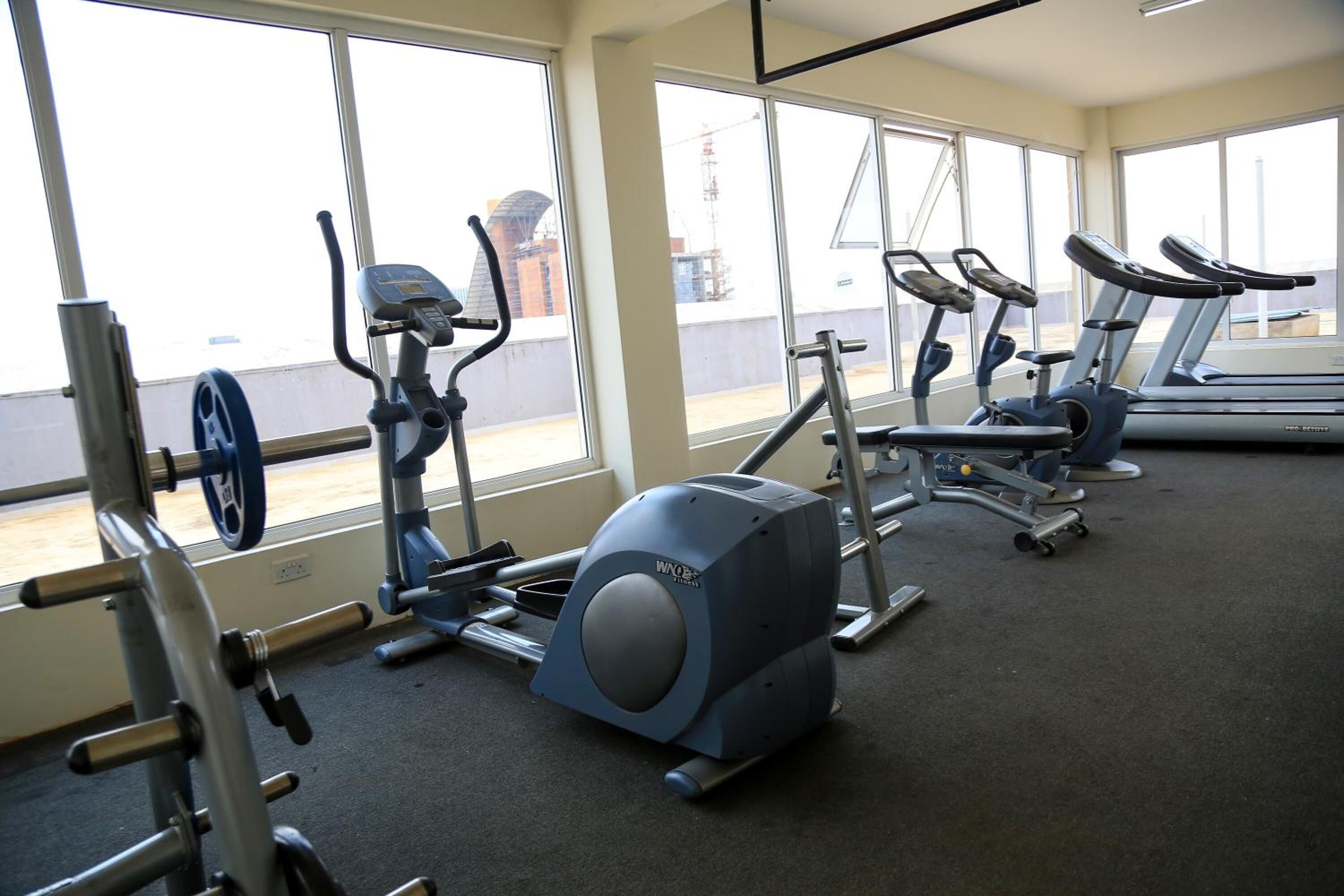 A gym with cardio machines, weight equipment, and large windows offering views of the outside.