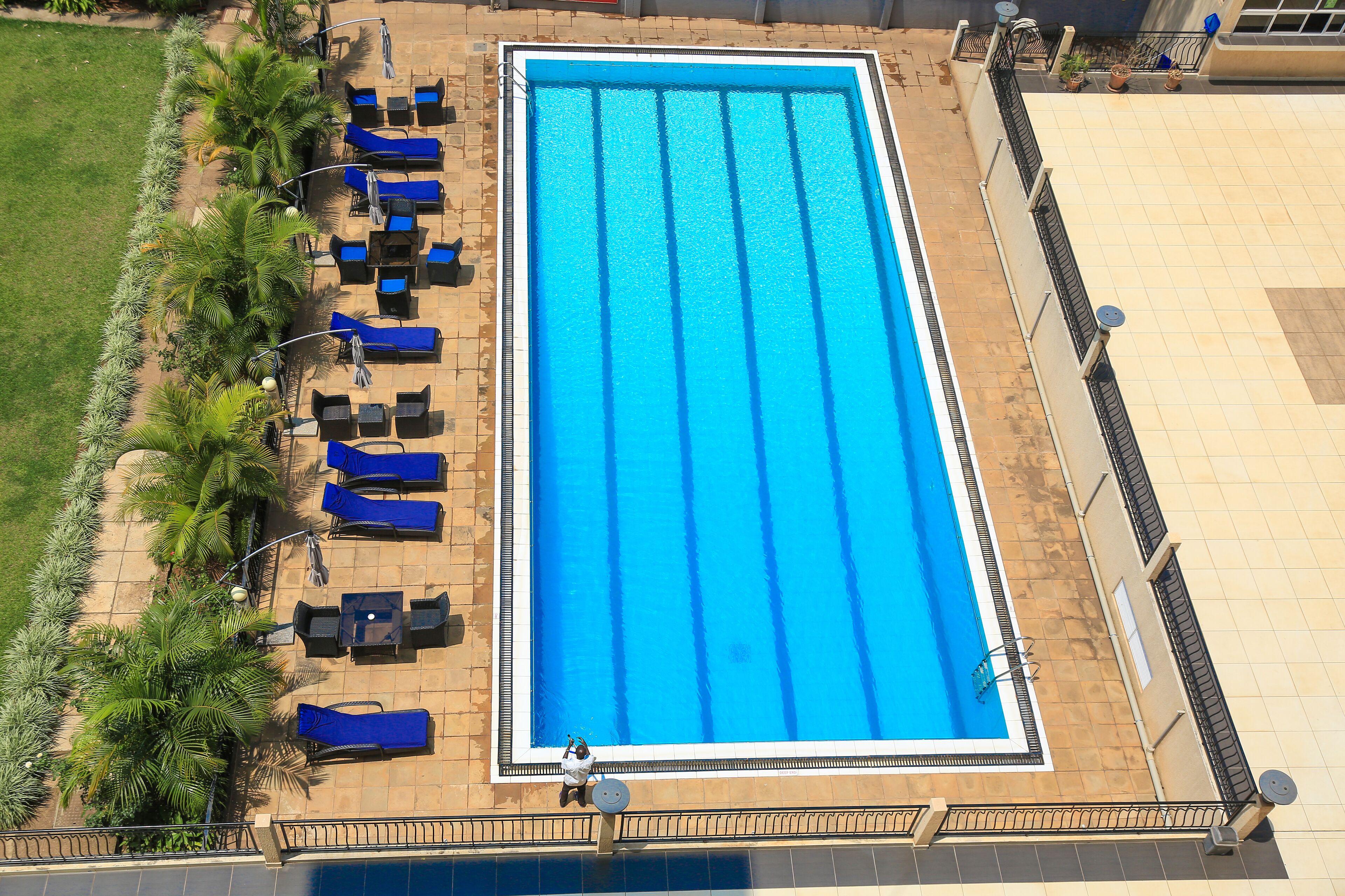 A rectangular swimming pool with blue water, surrounded by lounge chairs and tables, and a tiled deck area.