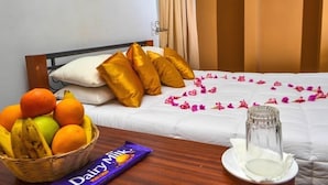 Una cama bien hecha con almohadas doradas, una cesta de fruta, una barra de chocolate y un vaso de leche sobre una mesa de madera.