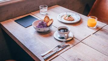 Une table en bois sur laquelle sont disposés des aliments pour le petit-déjeuner, notamment du pain, un saladier rempli de salade, une tasse de café et un verre de jus d’orange.