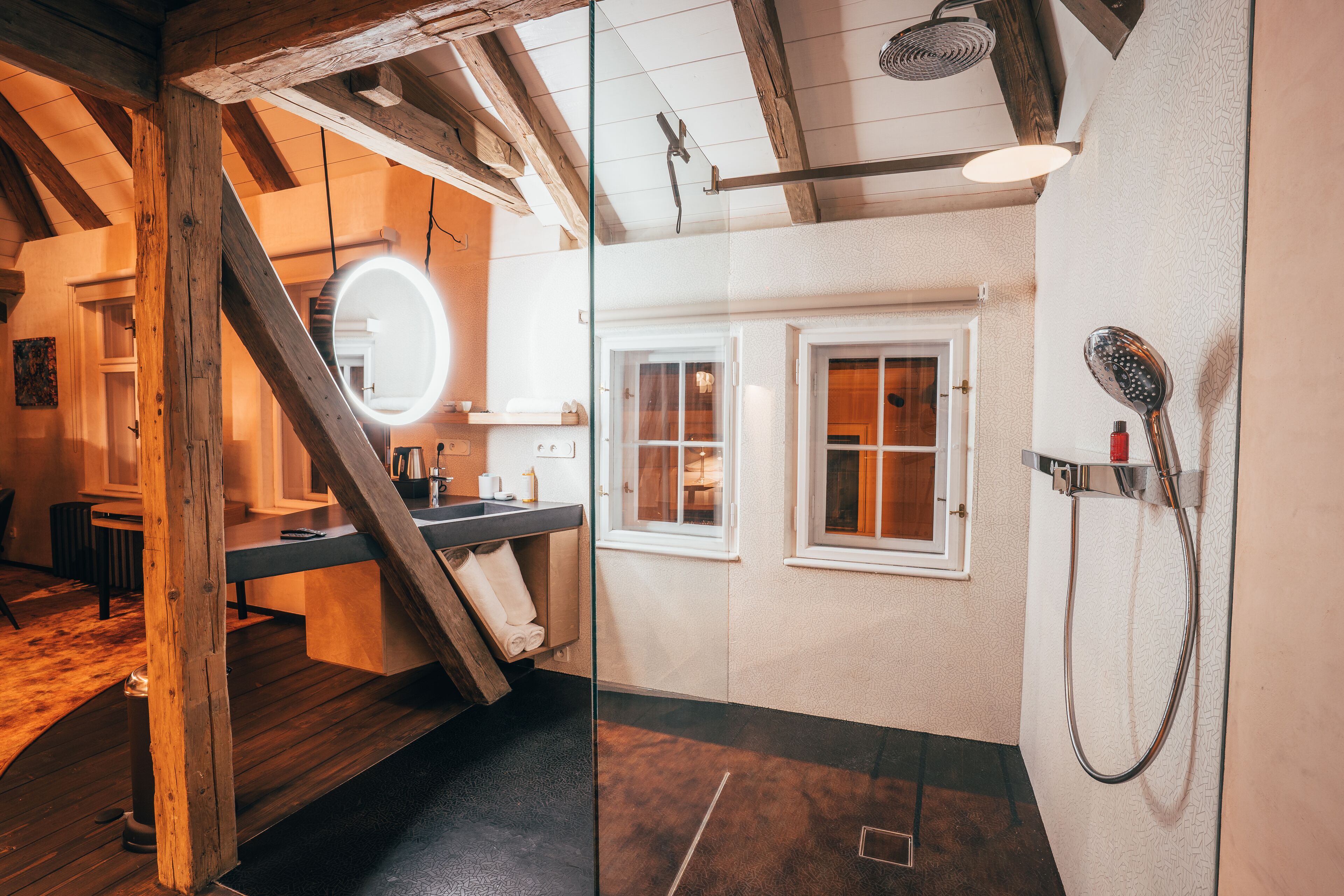Uma casa de banho moderna com escada de madeira, espelho redondo, chuveiro e janela.