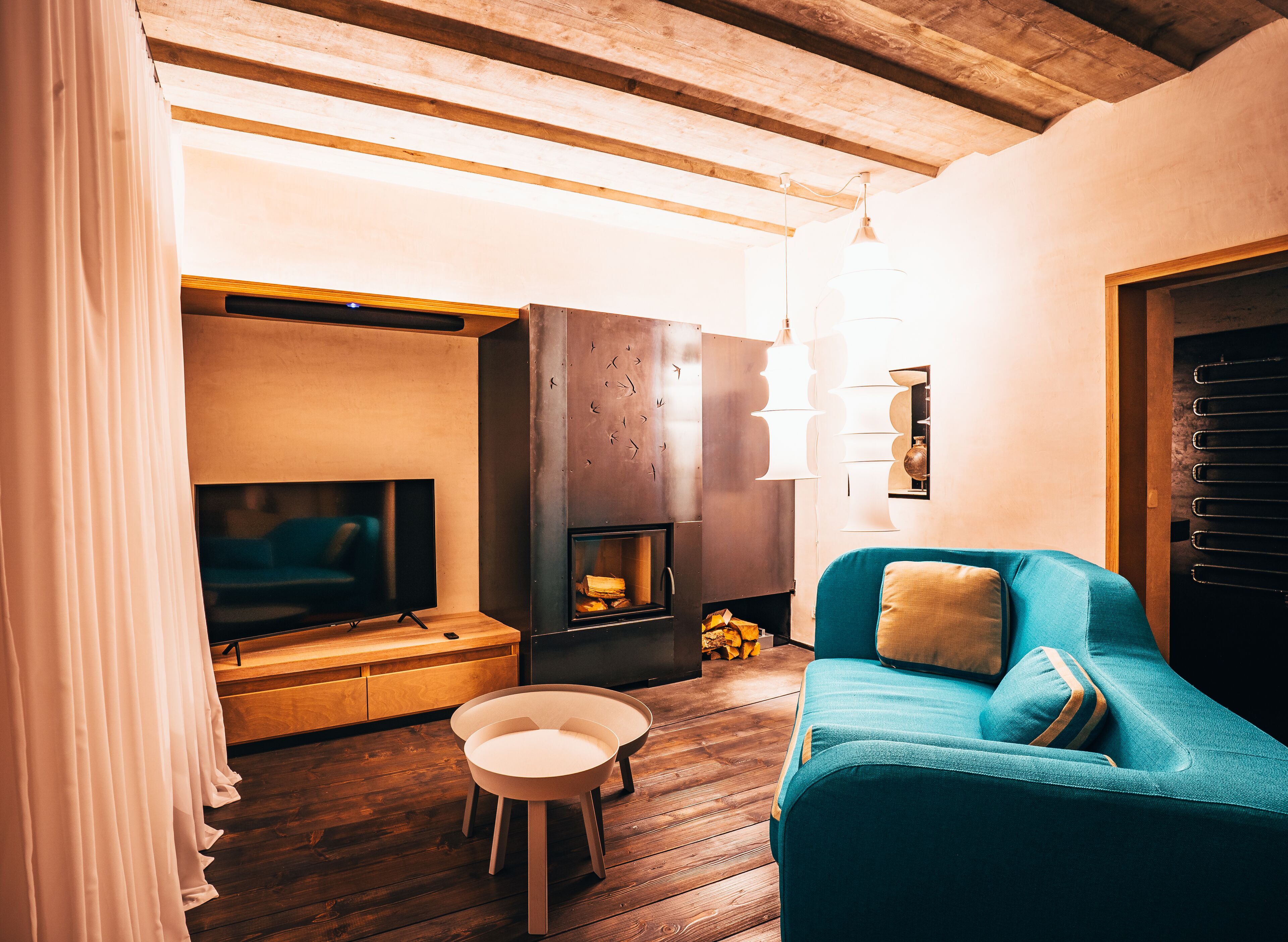 Een gezellige woonkamer met een houten plafond, een open haard, een blauwe bank en een televisie.