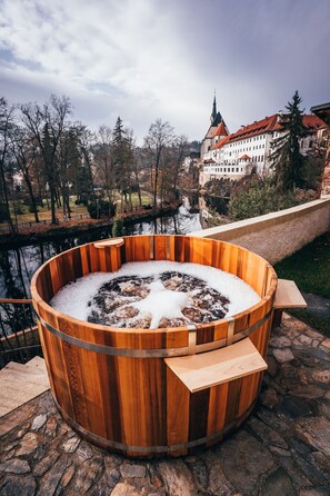 Un jacuzzi de madera con un camino de piedra y una vista de un castillo al fondo.