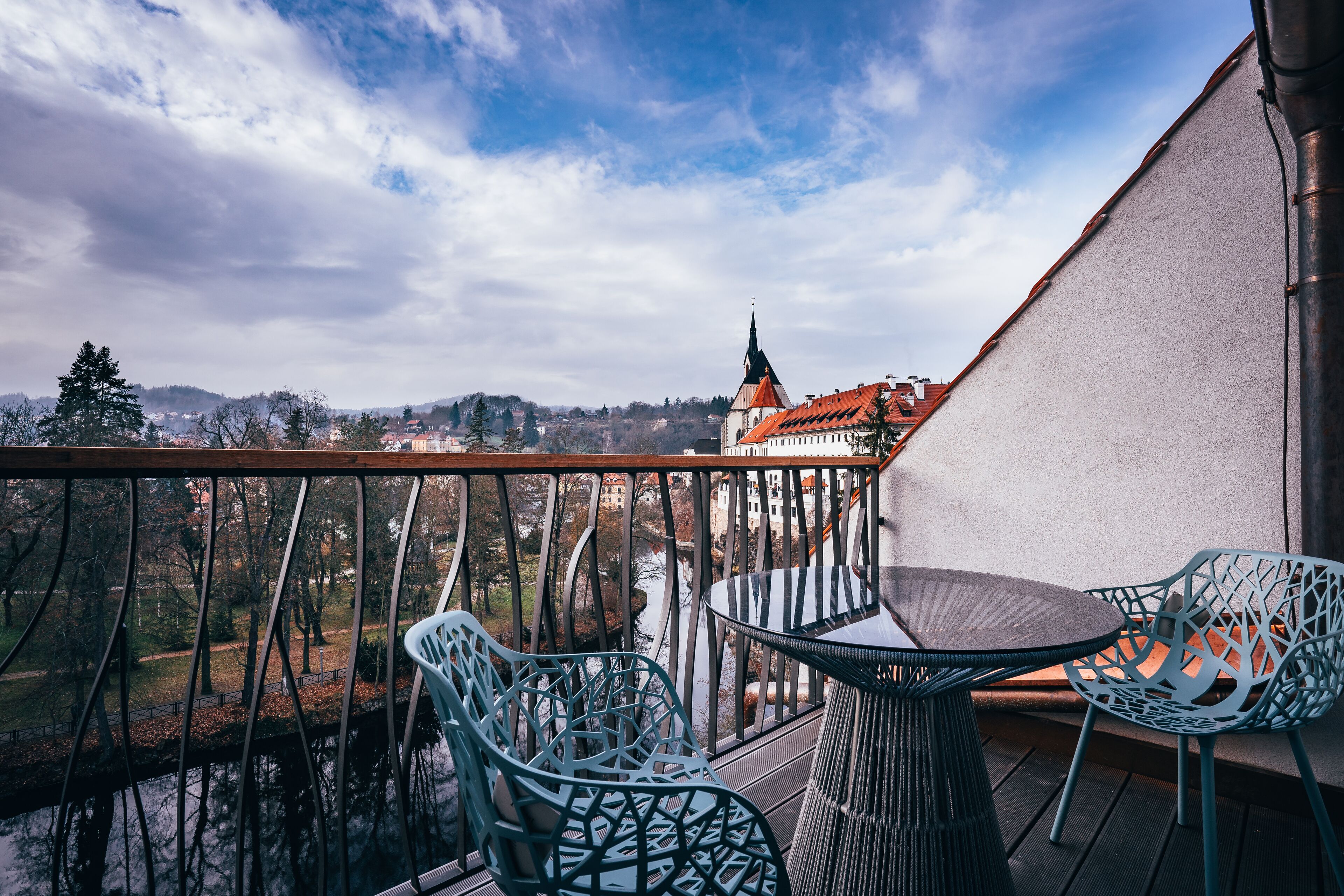 A balcony with a table and chairs, overlooking a town with a prominent church spire.