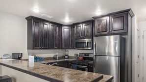 A modern kitchen with dark wood cabinets, stainless steel appliances, granite countertops, and bar stools. - Moab Adventure Condo Near Arches | Pool & Hot Tub (Moab)