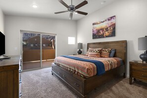 A bedroom with a bed, a ceiling fan, a window, and a door leading to a balcony. - Moab Adventure Condo Near Arches | Pool & Hot Tub (Moab)