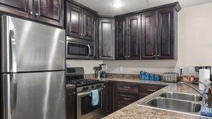 A kitchen with dark wooden cabinets, stainless steel appliances, granite countertops, and a double sink. - Redrock Retreat by National Parks | Pool & HotTub (Moab)