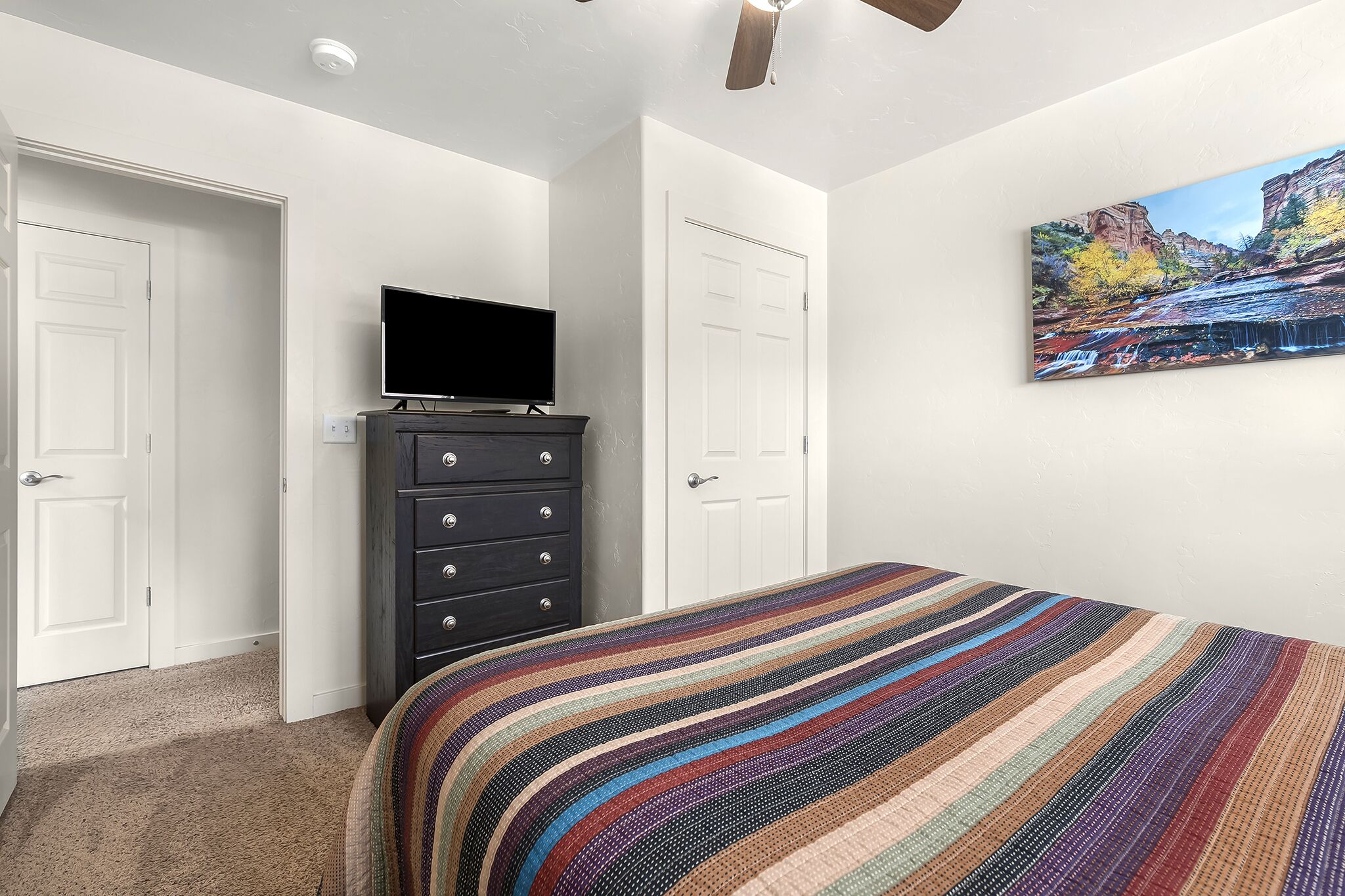 Une chambre à coucher avec un lit, une commode, un téléviseur et un tableau accroché au mur.