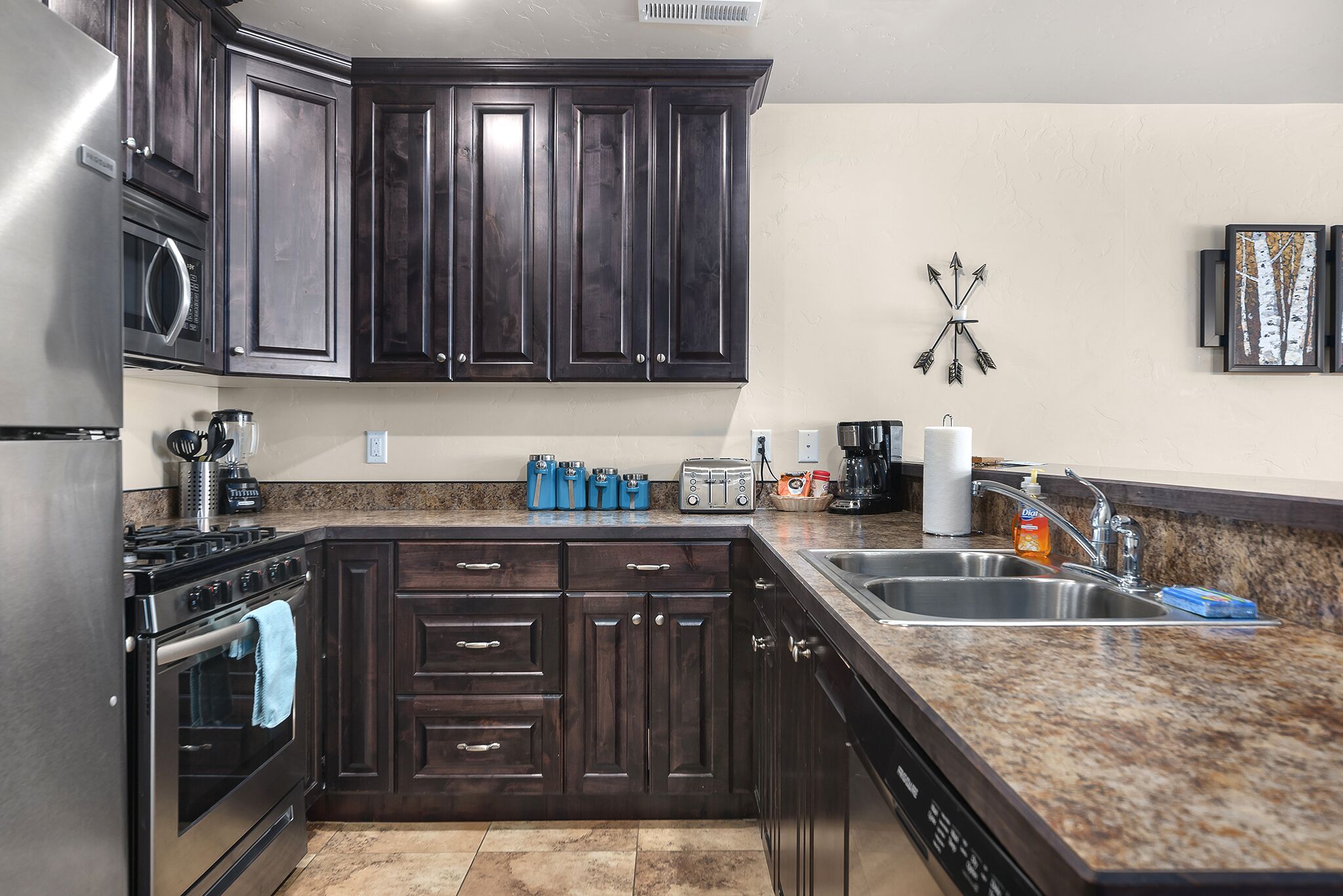 A kitchen with dark wood cabinets, a stainless steel refrigerator, a microwave, a stove, and a granite countertop.