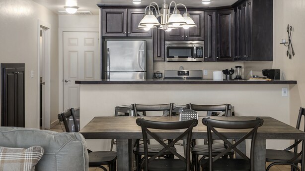 A modern kitchen with dark cabinets, stainless steel appliances, and a central island with seating. - Redrock Retreat by National Parks | Pool & HotTub (Moab)