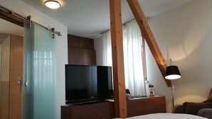 A hotel room with a bed, a flat-screen TV, a wooden desk, a lamp, and a sliding door.