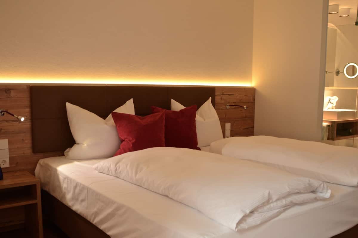 Een hotelkamer met een houten hoofdeinde, een nachtkastje en een spiegel met verlichting.