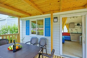A covered patio with a table set for dining, a bottle of wine, and a fruit bowl. - Camping Adria Mobile Homes in Brioni (Pula)