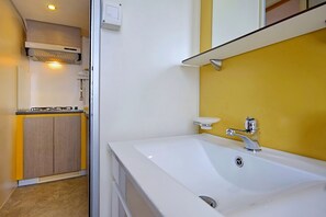 A modern bathroom with a white bathtub, a yellow wall, and a kitchen area with a built-in cabinet and stove. - Camping Adria Mobile Homes in Brioni (Pula)