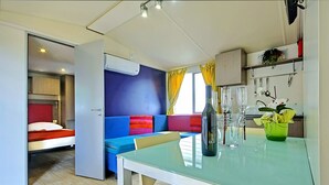 Ett modernt rum med ett glasbord, en soffa, en säng och en köksdel med en hylla.