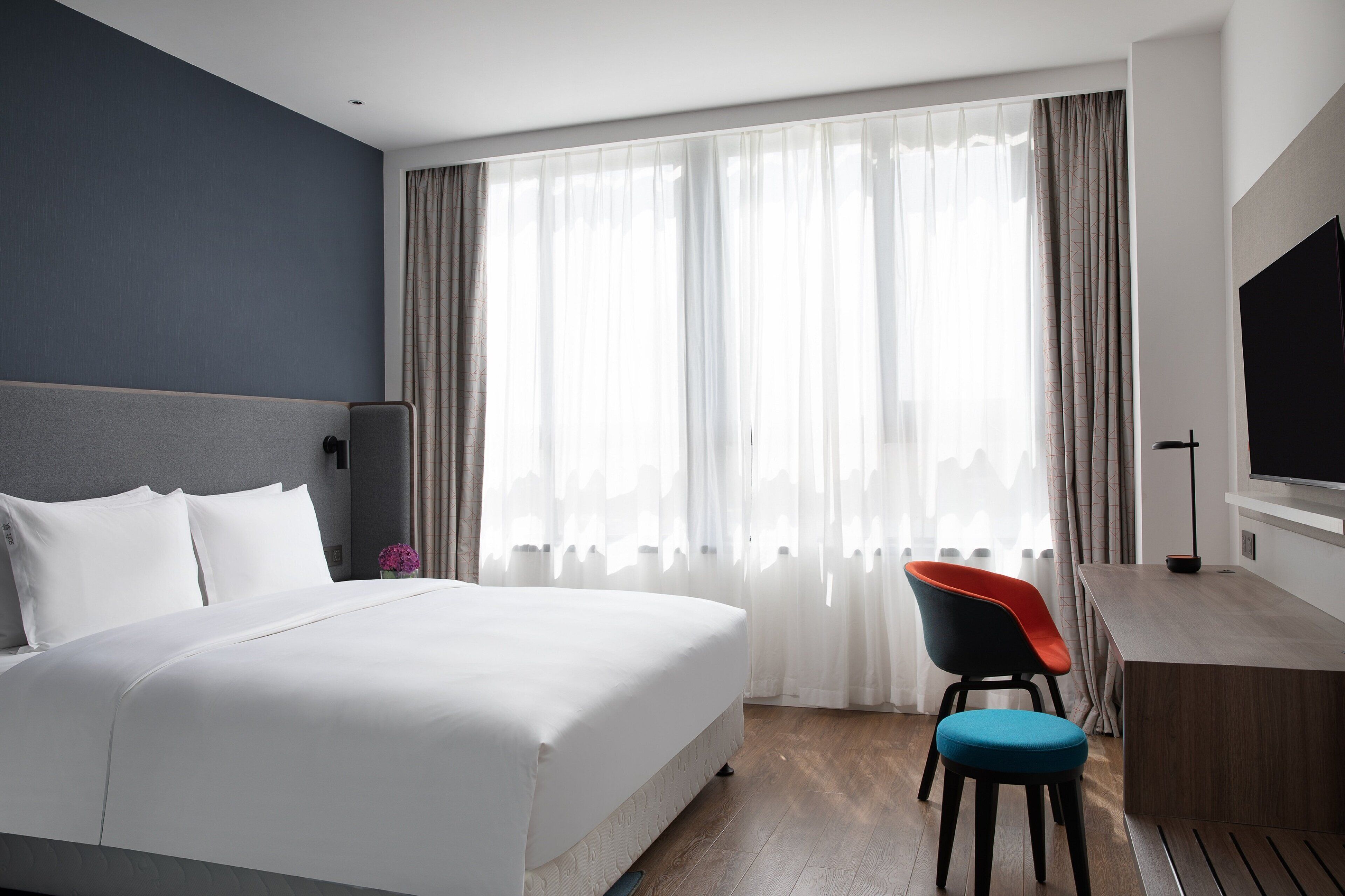 A hotel room with a large bed, a desk with a chair, a television, and a window with curtains.