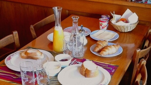 A breakfast table set with croissants, a bottle of orange juice, and various condiments.