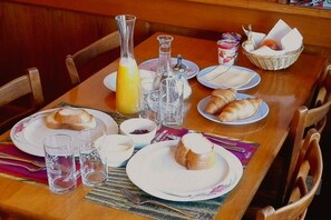 Mesa de pequeno-almoço posta com croissants, sumo de laranja e vários acompanhamentos.