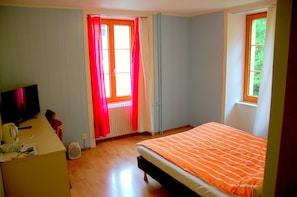 Quarto com cama, escrivaninha, cadeira, radiador e janela com cortinas.